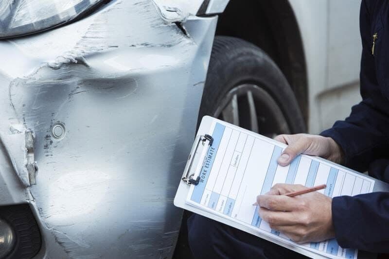 A technician reviewing collision damage with a clipboard next to a damaged car
